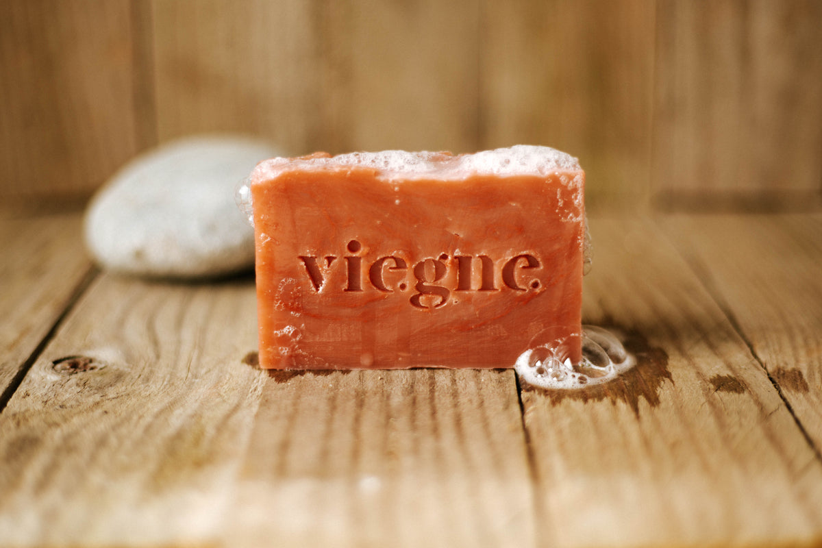 savon naturel bio sans emballage zéro déchet posé sur planche de bois, couleur rouge ocre naturelle, mousse généreuse sur le savon. savon issu de la vigne, enrichi aux polyphénols et aux arômes des cépages.